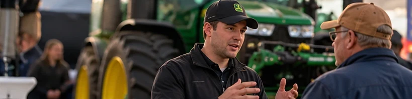 An equipment rep talking with a farmer in front of a tractor at a farm show.